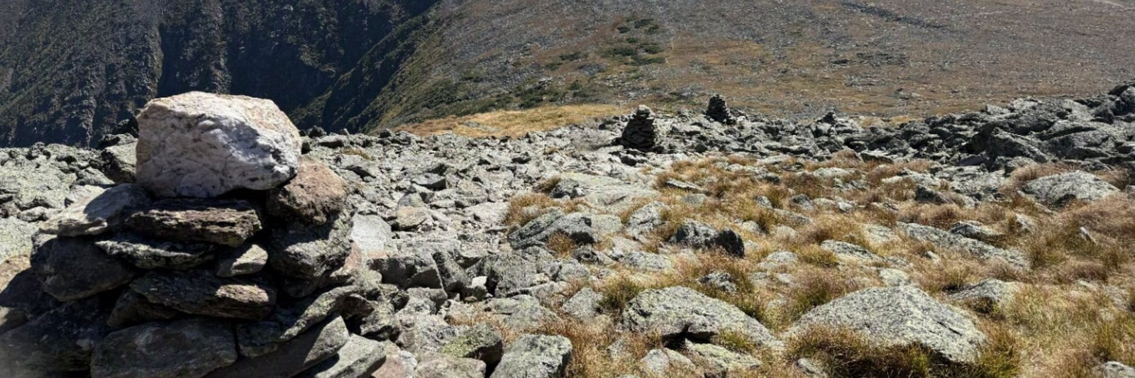 Stone cairn topped with a pale quartz boulder on a rocky White Mountains ridge, with a second cairn and open alpine slopes beyond